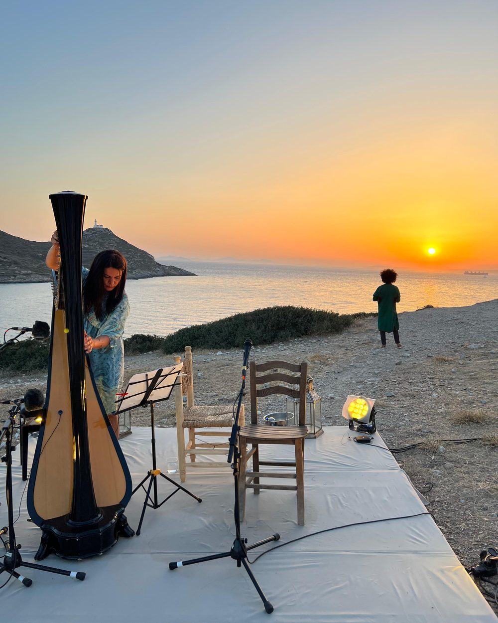 A harpist playing on the shore at sunset, a guest watching the sun go down