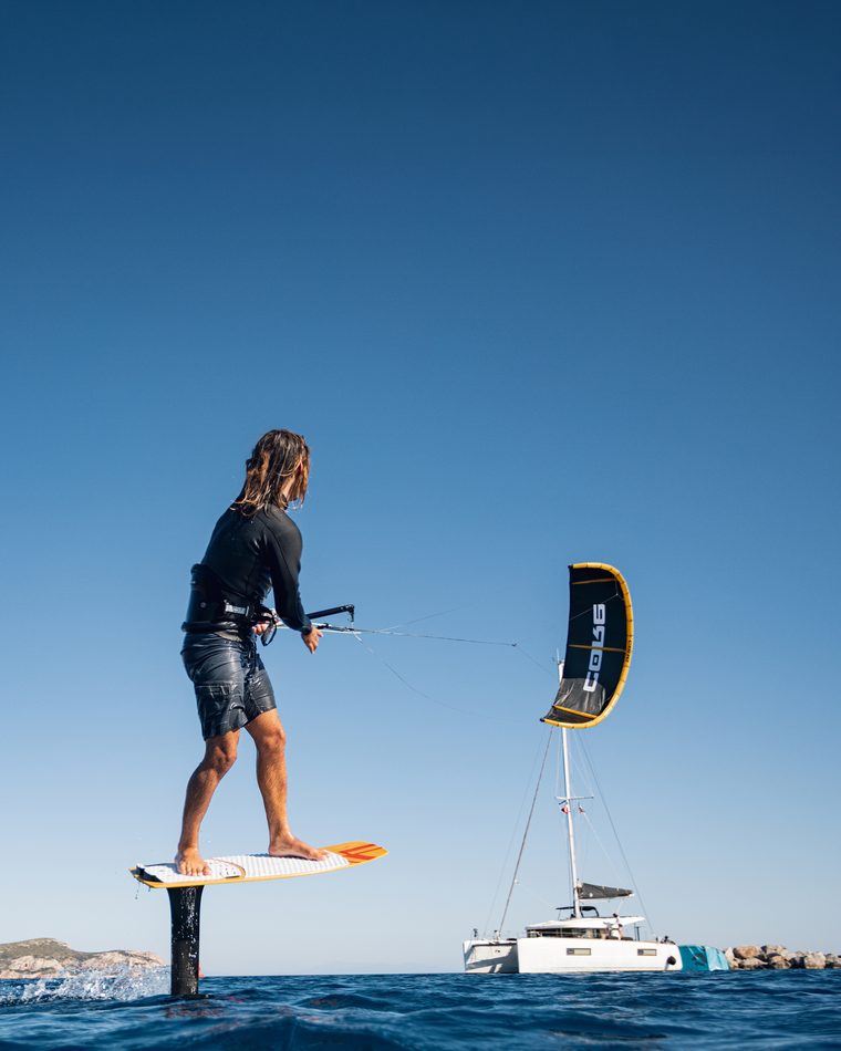 A kite foiler riding past the anchored catamaran