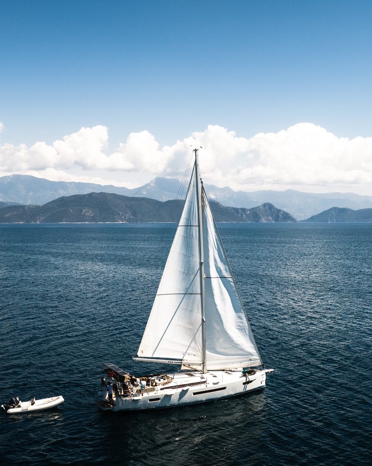 A sailing yacht under full canvas, the Aegean coast behind