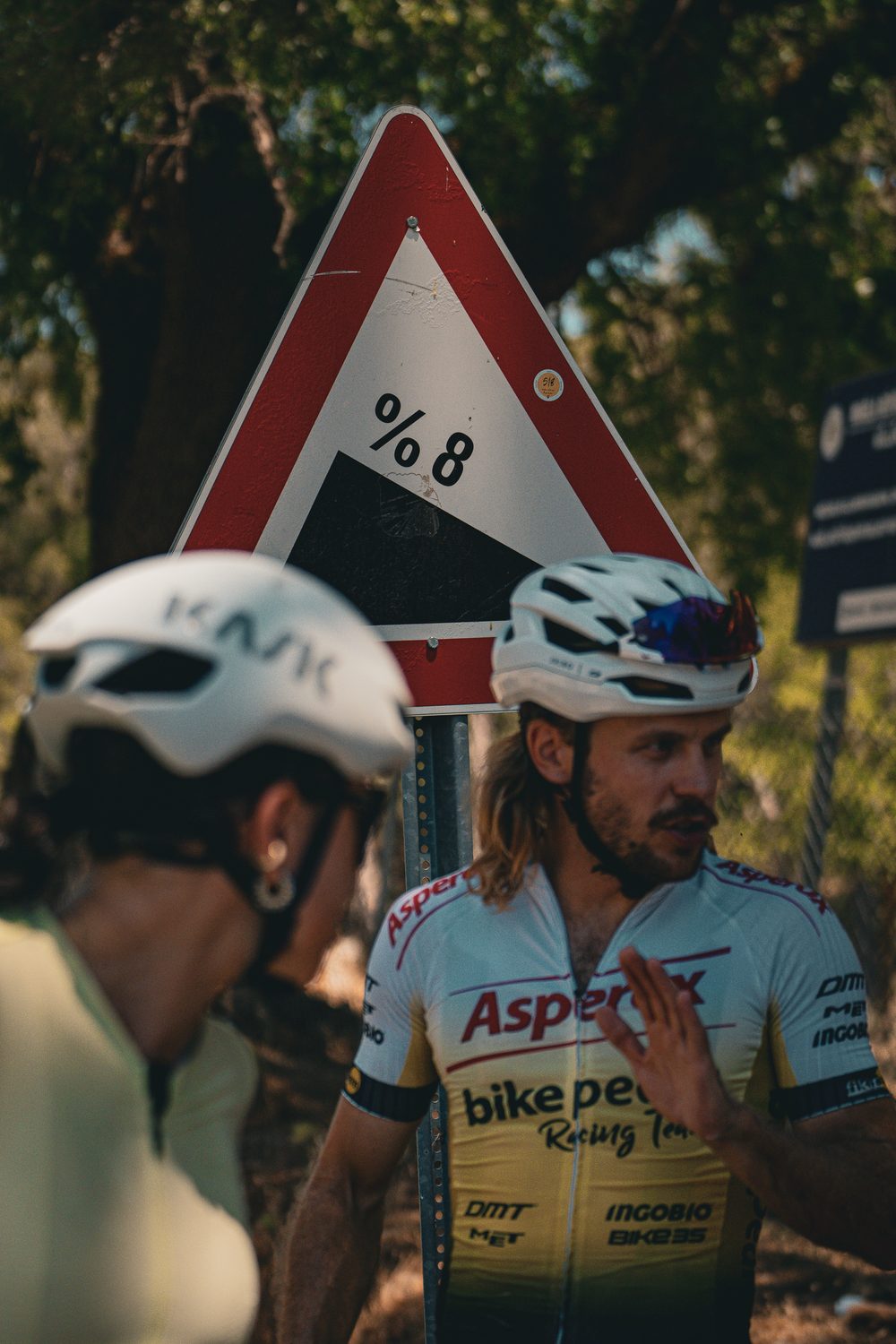Two riders talking beside an 8% gradient sign